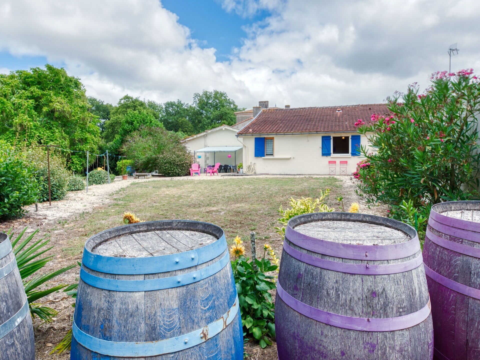 A rustic house with a garden, surrounded by wooden barrels.