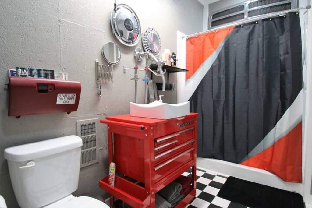 A compact bathroom with a toilet, a red tool chest, a sink, and a shower curtain.
