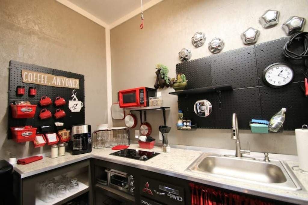 A compact kitchen with a pegboard wall displaying kitchen utensils, a microwave, and a clock.