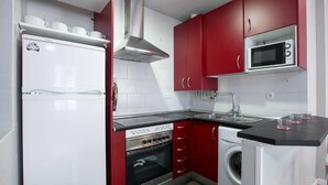 Une cuisine de taille réduite avec des placards rouges, un réfrigérateur blanc, un four à micro-ondes, une cuisinière et un lave-linge.