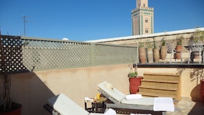 A rooftop terrace with two lounge chairs, a small table with a hat and a bottle, and potted plants. - RIAD ET SPA MISRIA LES OLIVIERS (Marrakech)