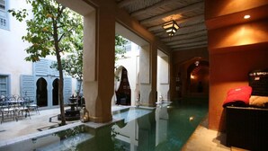 An indoor swimming pool with a tiled floor, a tree, and a seating area with a red towel. - RIAD ET SPA MISRIA LES OLIVIERS (Marrakech)