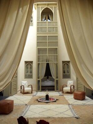 Une pièce dotée d’une grande fenêtre en arc de cercle, de deux chaises, d’une petite table ornée d’un objet décoratif et d’un grand tapis sur le sol.