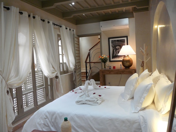 Une chambre d’hôtel avec un lit bien fait, des rideaux blancs, une tête de lit en bois, une lampe de chevet et un tableau encadré au mur.