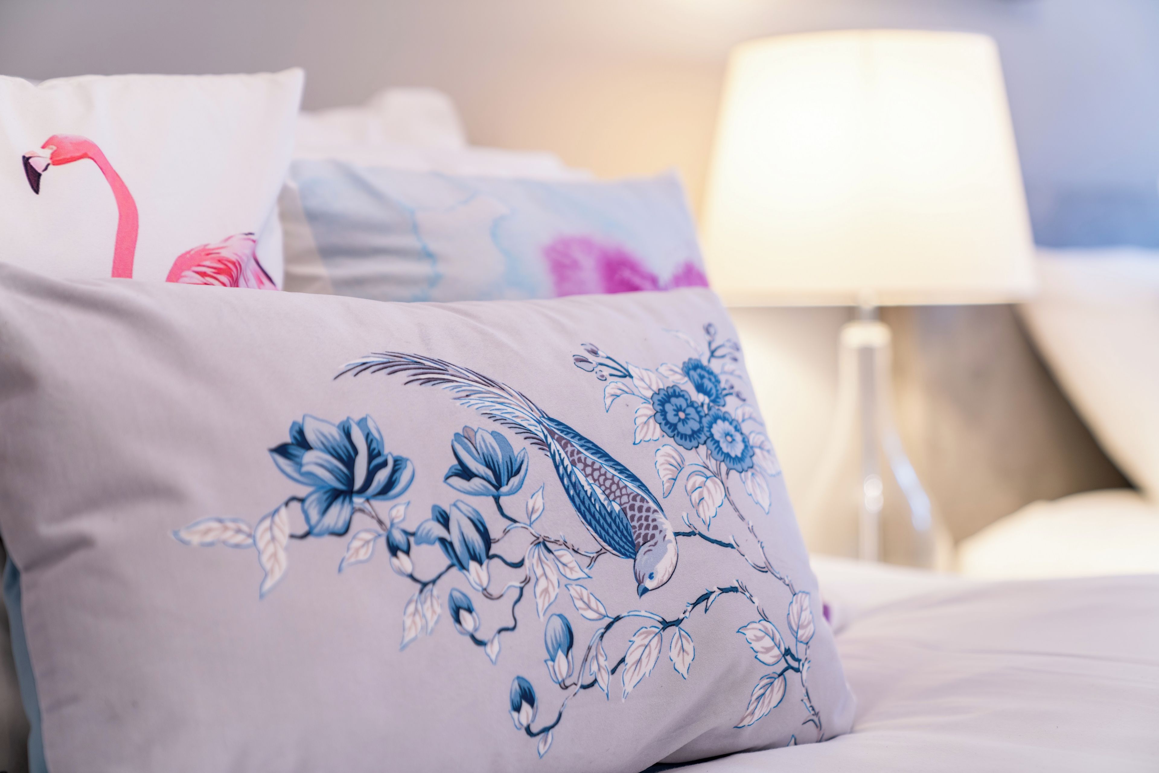 Cama com travesseiros decorativos com motivos florais e de pássaros.
