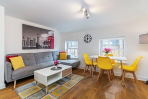 Een moderne woonkamer met een grijze bank, een witte salontafel en een eethoek met gele stoelen.