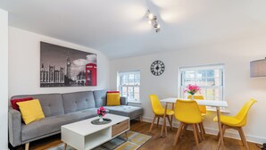 A modern living room with a grey sofa, yellow chairs, a white coffee table, and a cityscape painting. - London Street, Andover, Hampshire, SP102NU, United Kingdom (Andover)