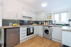 Een moderne keuken met witte kastjes, roestvrijstalen apparatuur en een houten aanrecht.