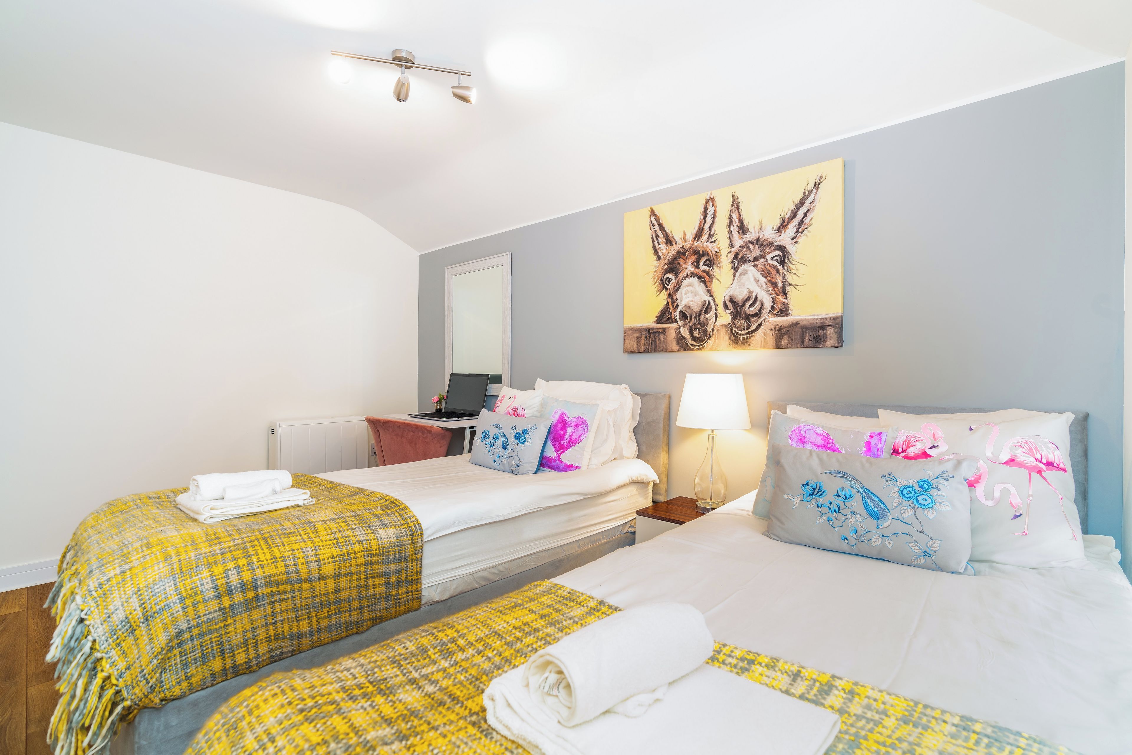 Habitación de hotel con dos camas, un escritorio, una computadora portátil y un cuadro de burros en la pared.
