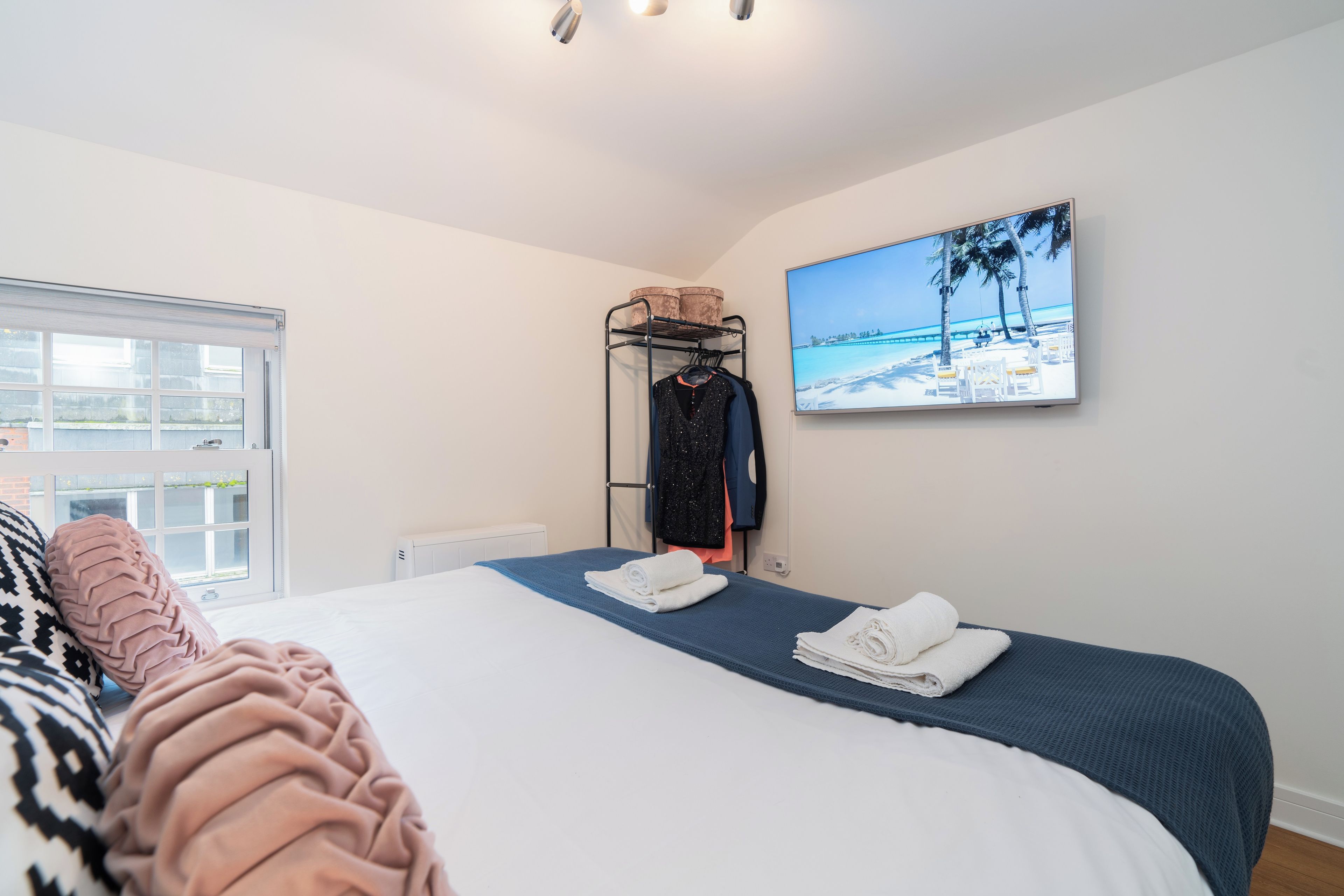 A bedroom with a bed, a wall-mounted TV, a clothing rack, and a window.