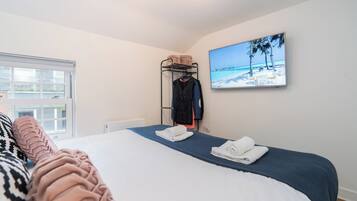 A bedroom with a bed, a wall-mounted TV, a clothing rack, and a window.