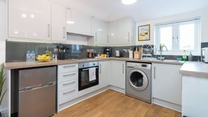 A modern kitchen with white cabinets, a stainless steel refrigerator, a built-in oven, a washing machine, and a window providing natural light. - London Street, Andover, Hampshire, SP102NU, United Kingdom (Andover)