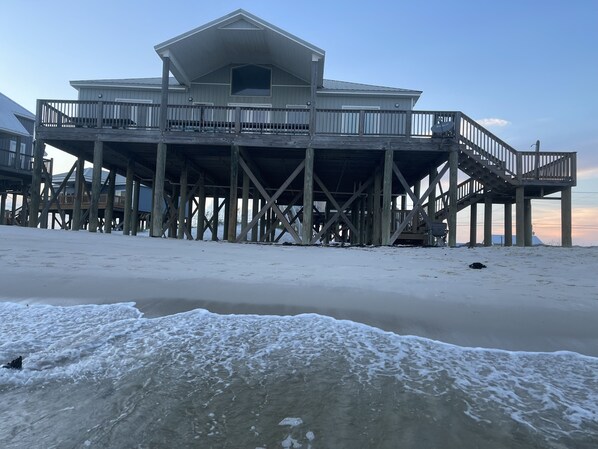 Una estructura de muelle de madera con un edificio grande sobre pilotes, un paseo techado y vistas a la playa.
