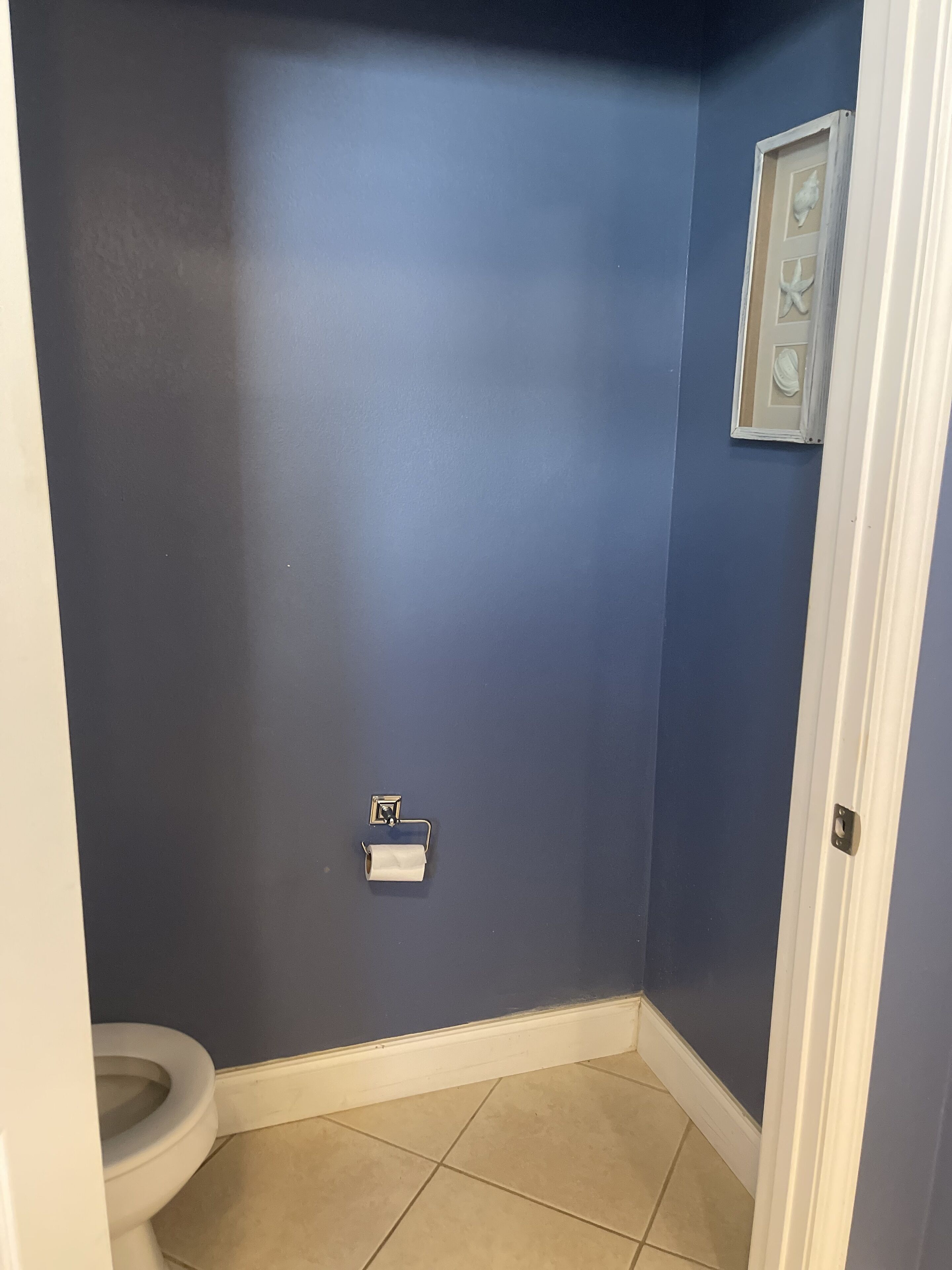 A bathroom with a toilet, a towel rack, and a framed picture on the wall.