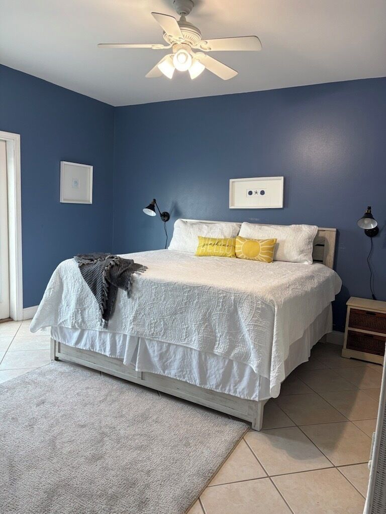 Un dormitorio con cama, ventilador de techo, mesita de noche y lámpara de pared.