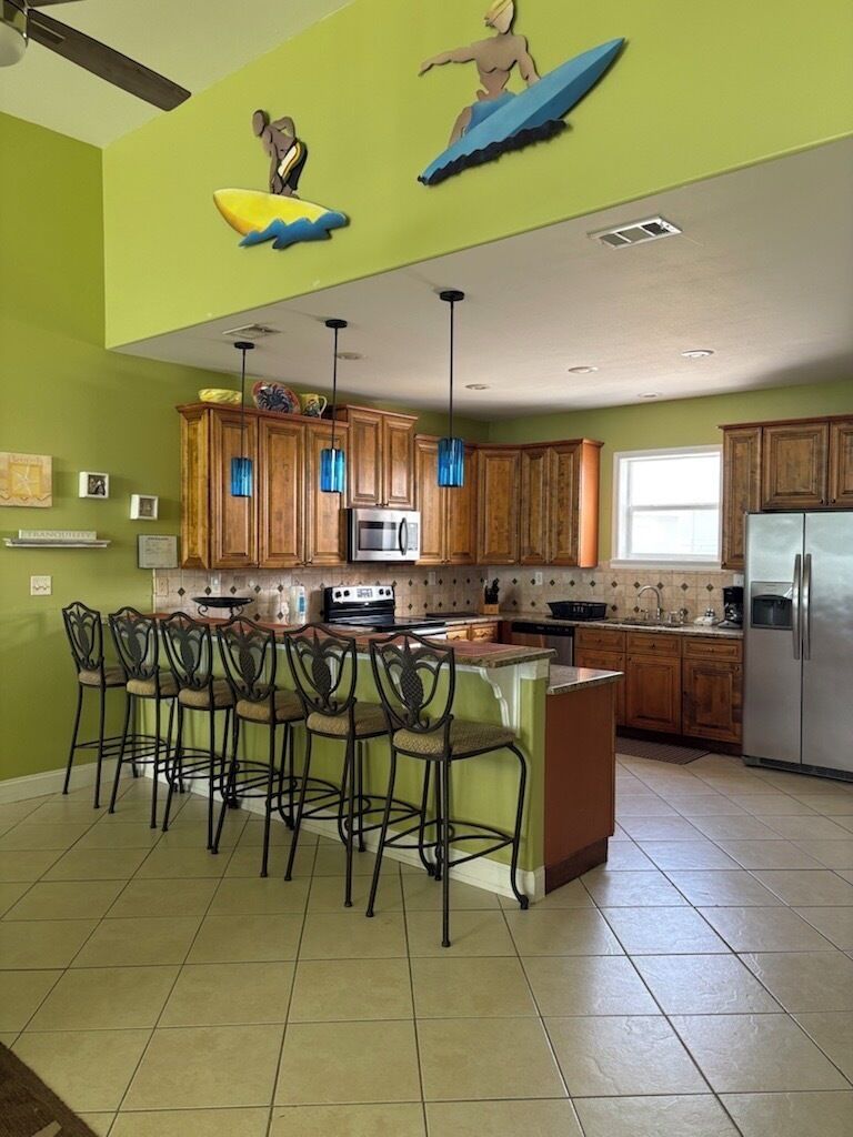 A kitchen with wooden cabinets, a central island with bar stools, and a ceiling fan.