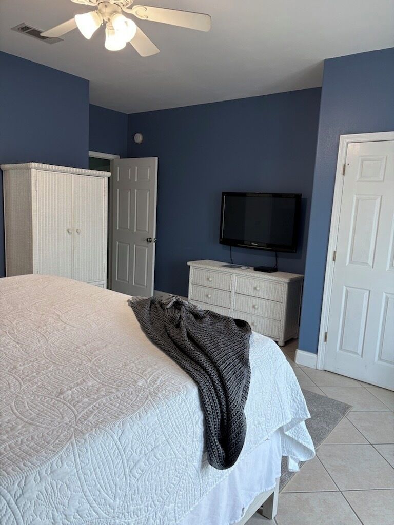 A bedroom with a bed, a television, a wardrobe, and a ceiling fan.