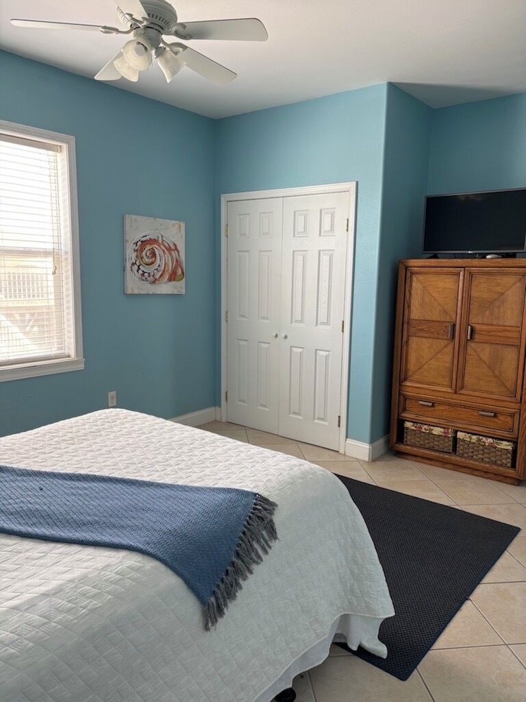 Un dormitorio con cama, ventilador de techo, armario, televisor y una puerta.