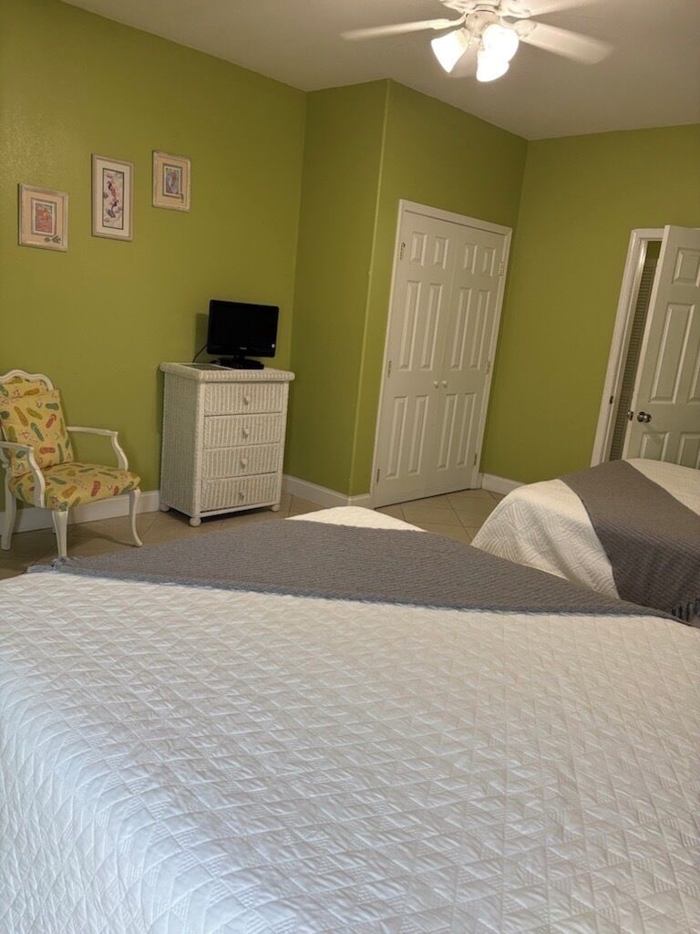 A bedroom with two beds, a white dresser, a television on the dresser, and a chair.