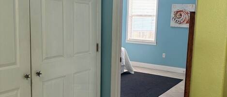 Un couloir avec une porte fermée, une fenêtre avec des stores et un tapis sombre sur le sol.
