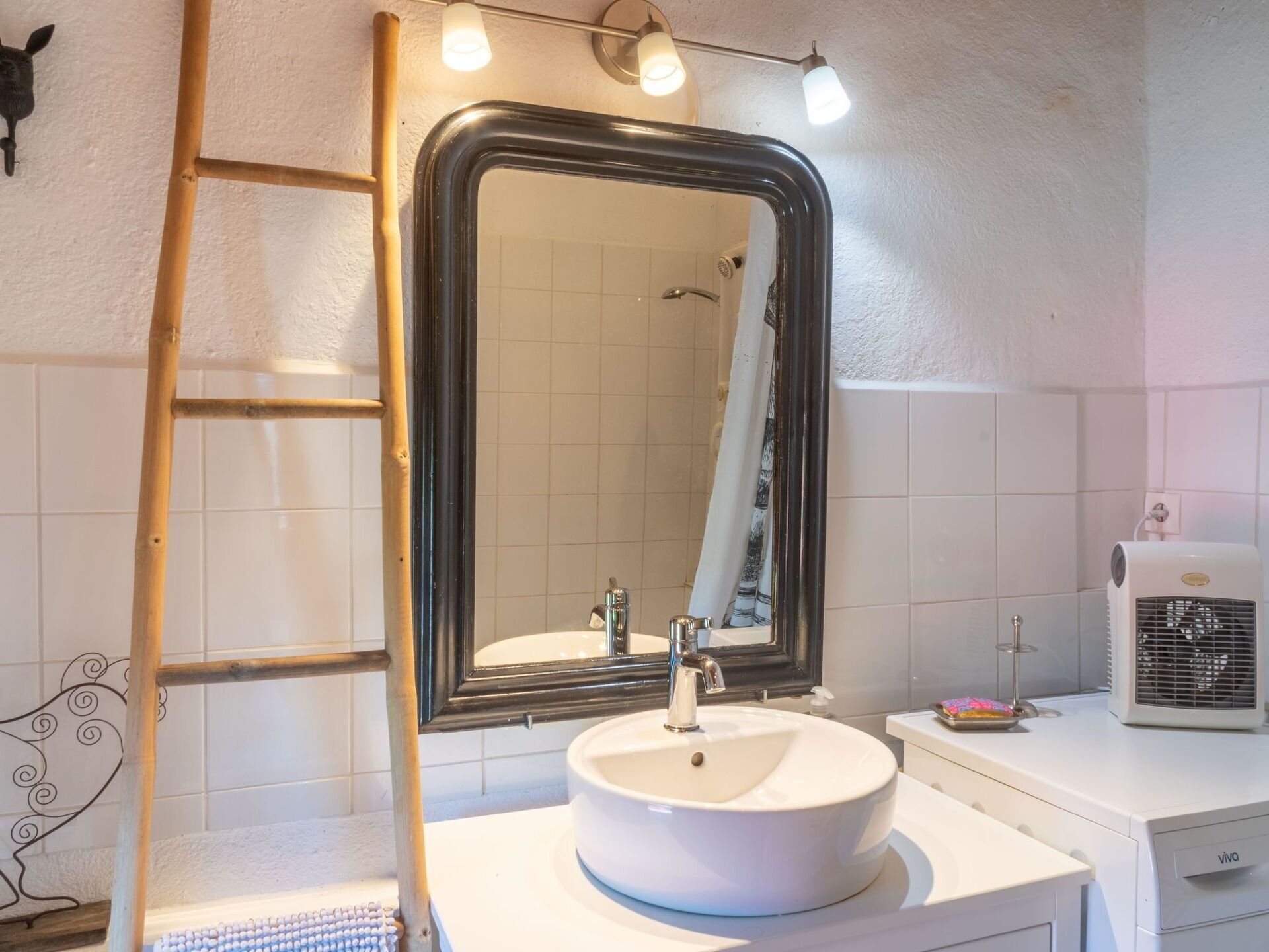 Une salle de bain avec un lavabo blanc, un miroir, un porte-serviettes, une douche et un radiateur blanc.