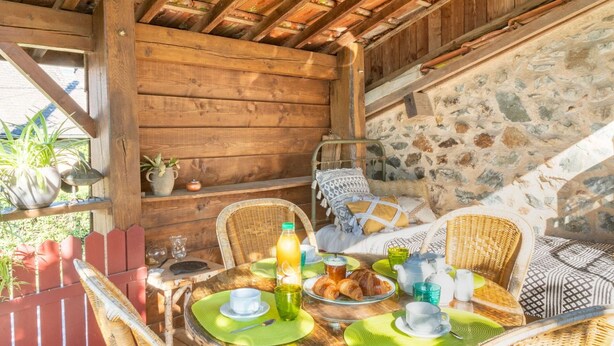 Un coin repas en bois, avec un mur en pierre, des chaises en osier et une table mise pour le petit-déjeuner.