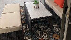 Un patio couvert aménagé avec des meubles en osier, une petite table ornée d’une plante et une vue sur un chantier de construction.