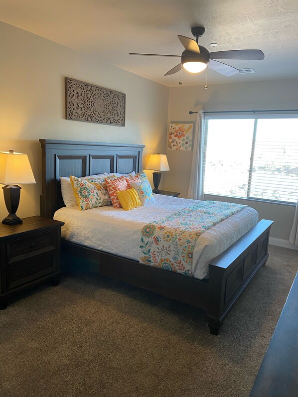A bedroom with a bed, two bedside tables, a ceiling fan, and a window with blinds.