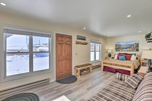 A cozy room with a wooden bed, a bench, and a view of a snowy landscape through large windows. - Walk to Marina: Rustic Grand Lake Retreat! (Grand Lake)