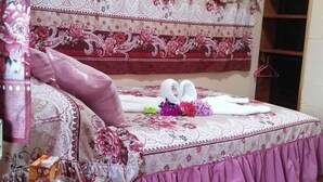 A bedroom with a bed covered in floral-patterned bedding, a bedside table with a glass, and a hanging chair. - Pensión y Cabinas Colibrí Monteverde B&B (Monteverde)