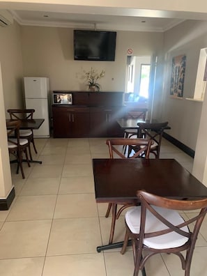 A dining area with a wooden table and chairs, a refrigerator, a microwave, and a television on the wall. - Fairview BnB (Umhlanga)