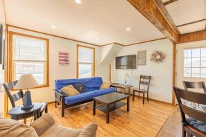A living room with a blue sofa, a wooden coffee table, a TV mounted on the wall, and a fireplace. - Steps from the ocean in the heart of Hampton Beach! (Hampton)