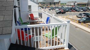 A balcony with white railings, a small table, and colorful chairs. - Steps from the ocean in the heart of Hampton Beach! (Hampton)