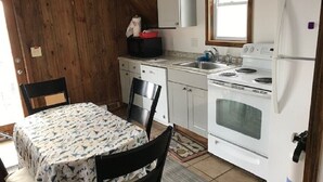 A compact kitchen with a stove, sink, and white cabinets. There is a dining table with chairs and a window above the sink. - Steps from the ocean in the heart of Hampton Beach! (Hampton)
