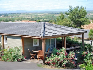 Ett litet hus med ett tak täckt av tegelpannor, en veranda med trämöbler och utsikt över ett lantligt landskap.