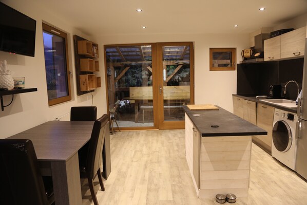 A modern kitchen with a built-in washing machine, a dining area with a table and chairs, and a sliding glass door leading to a balcony.