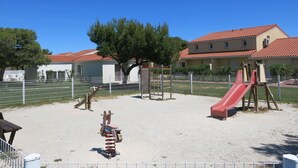A playground with a slide and swings, surrounded by a fence and trees. - Lovely apartment in villa for 4 guests with WIFI, A/C, pool, TV, patio and pets allowed (Torreilles)