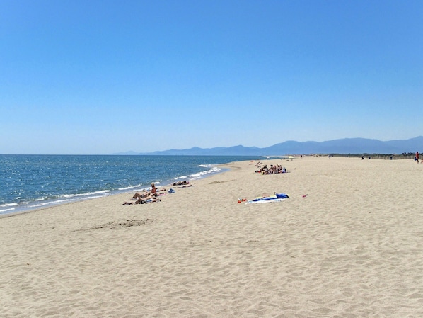 A wide sandy beach with a clear blue sky and distant mountains.