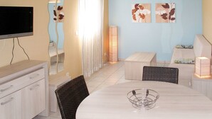 A modern living room with a flat-screen TV, a dining table with chairs, a sofa, and a lamp. - Lovely apartment in villa for 4 guests with WIFI, A/C, pool, TV, patio and pets allowed (Torreilles)