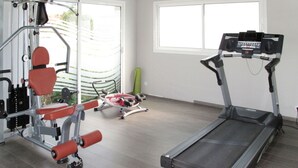 Un gimnasio con cinta de correr, máquinas de pesas y una colchoneta verde.