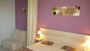 Un dormitorio con una cama, una mesita de noche, una lámpara, una silla y una pared decorada con tres cuadros.