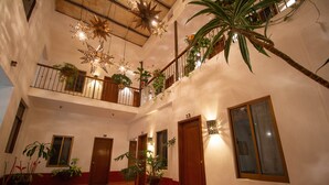 Un vestíbulo de hotel de varios niveles con una escalera central, varias puertas y plantas en macetas.