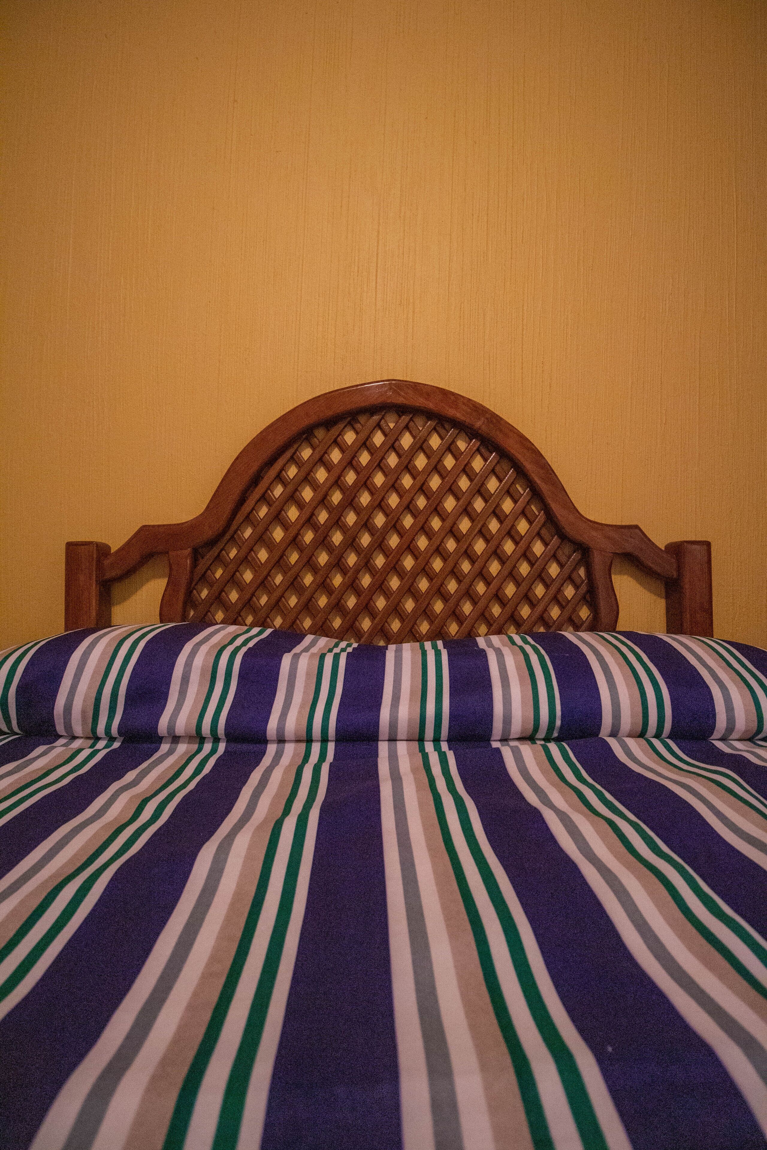 Una cama con cabecera de madera y colcha a rayas.