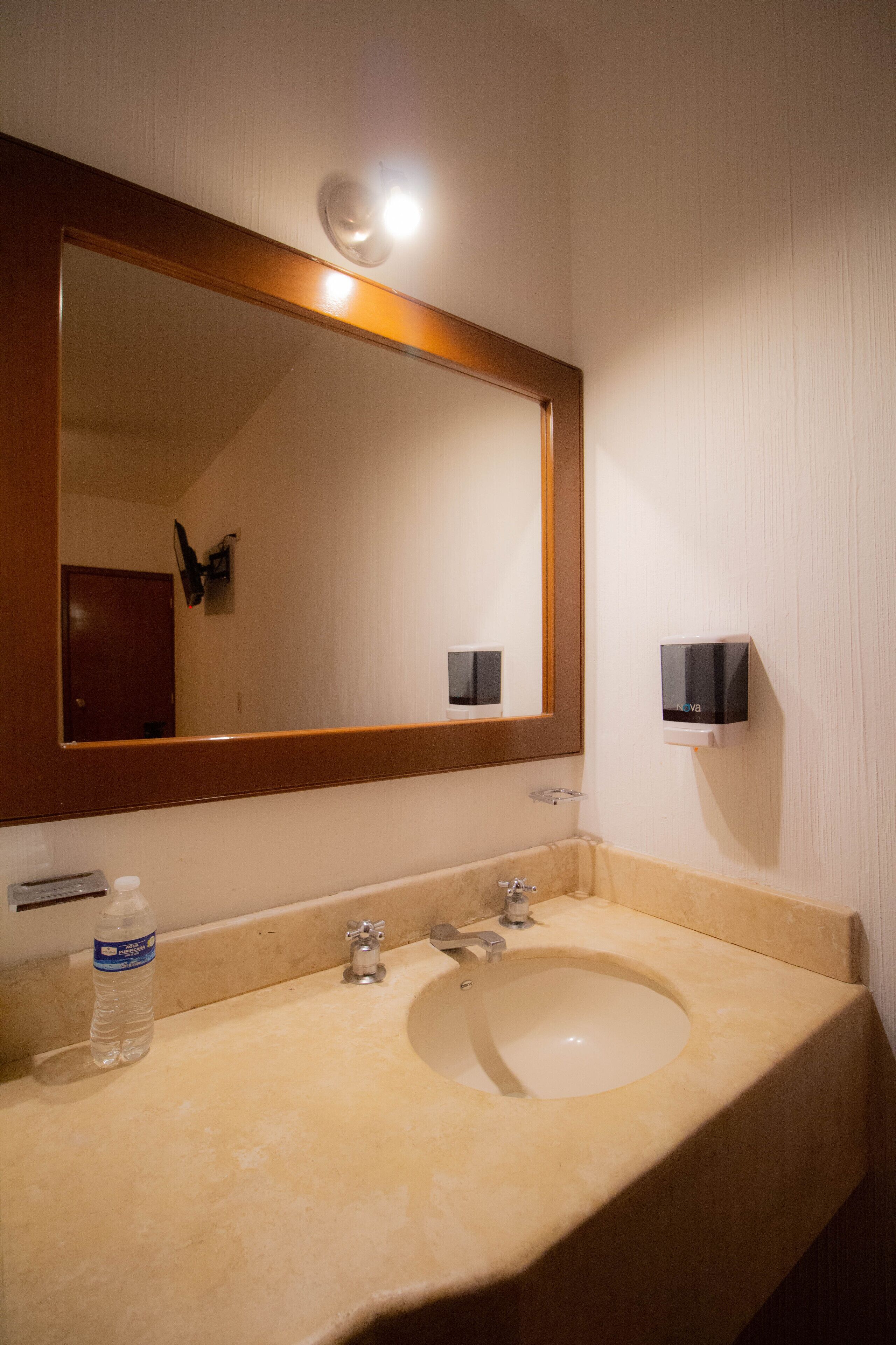 Un baño con un lavabo color beige, un espejo grande y un dispensador de jabón en la pared.