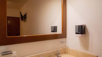 Un baño con un lavabo color beige, un espejo grande y un dispensador de jabón en la pared.