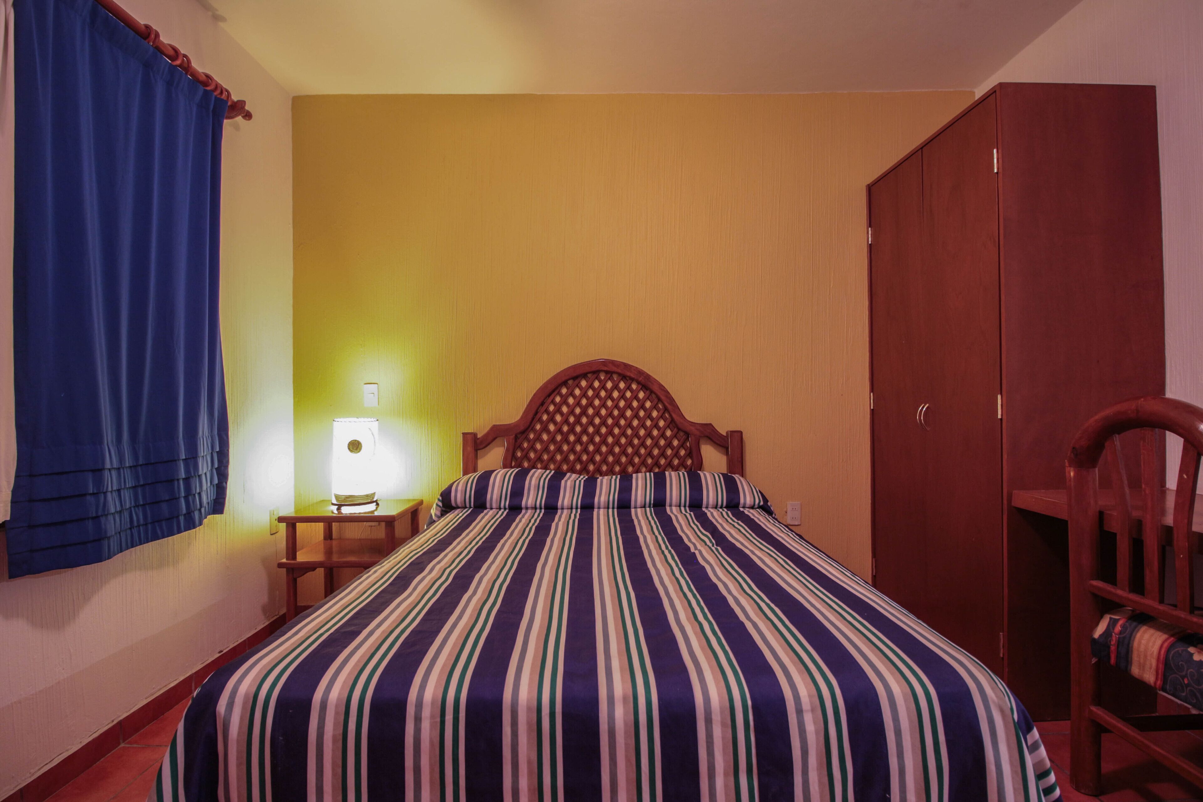 Une chambre avec un lit, une armoire en bois, une table de chevet avec une lampe et un rideau bleu.