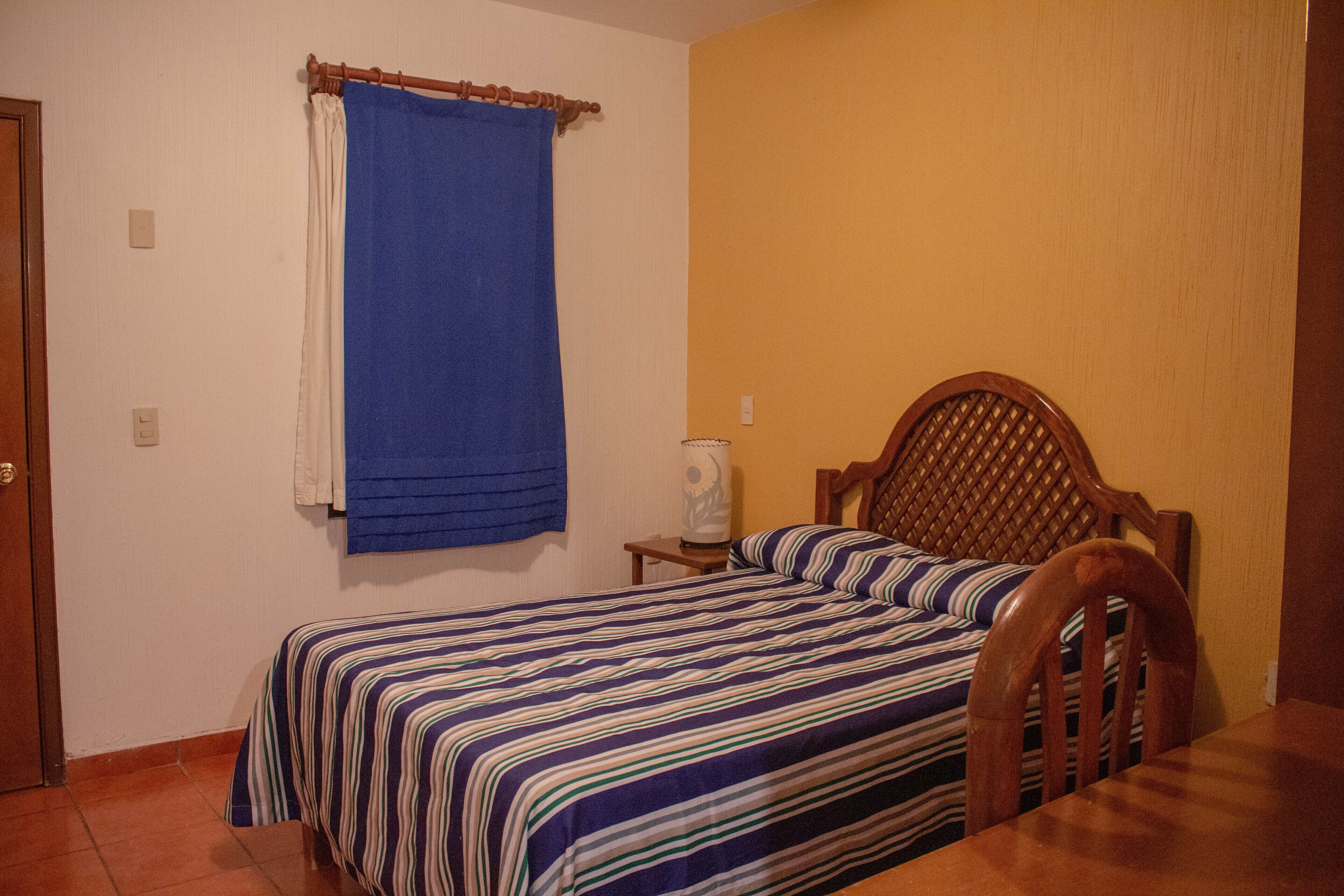A bedroom with a bed, wooden headboard, a nightstand, and a blue curtain.