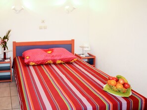 A hotel room with a bed, a nightstand with a lamp, a wall socket, and a fruit basket on the nightstand. - Beautiful apartment in villa for 6 guests with pool, TV, terrace and pets allowed (Saint-cyprien-plage)