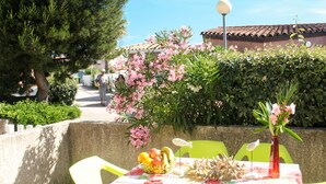 Un área de comedor al aire libre con una mesa y sillas, rodeada de follaje y flores.