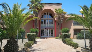 Un edificio con una amplia entrada arqueada, palmeras y un letrero que dice 'Grand Bleu Residences de Tourisme Les Jardins de Neptune'.